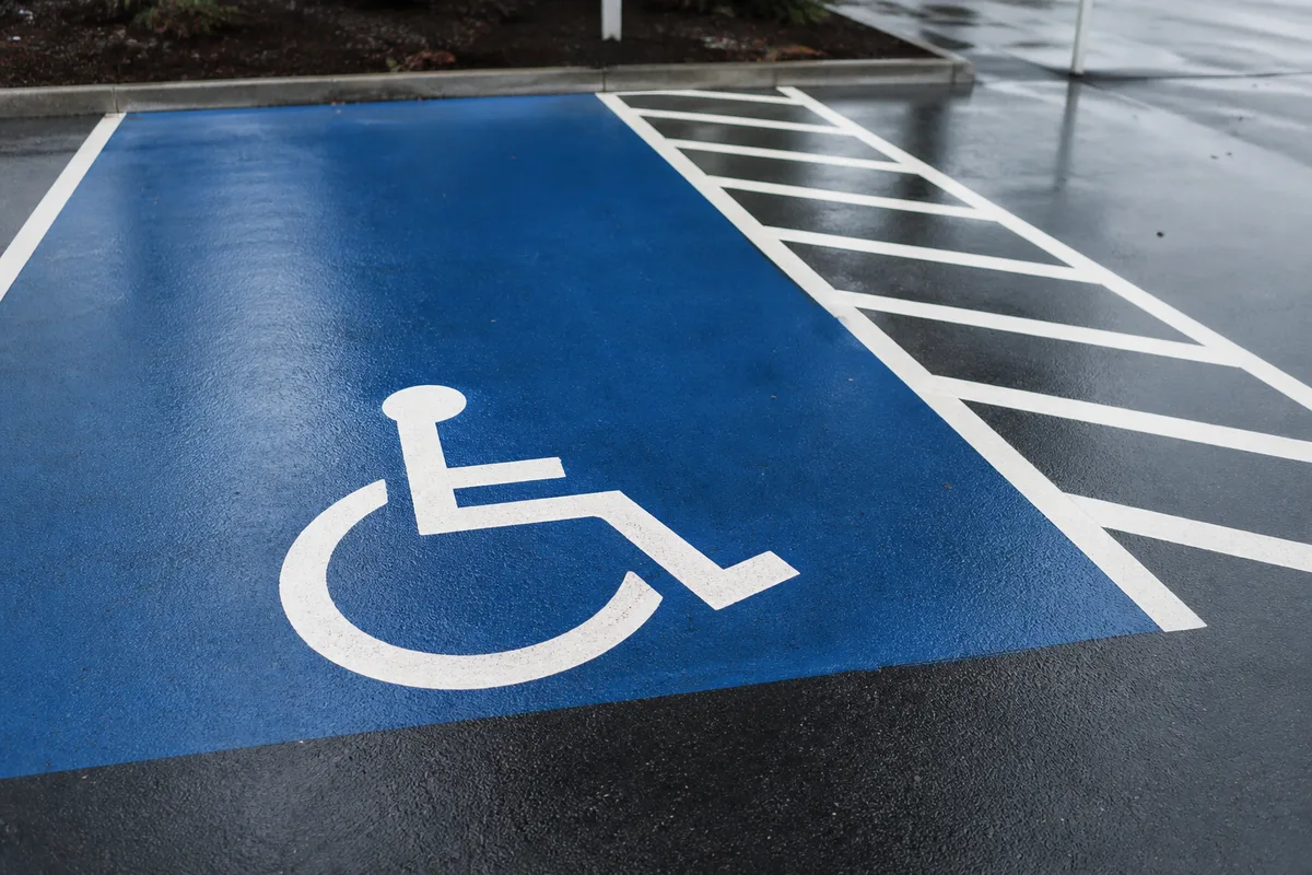 Détail au sol d&rsquo;une place de stationnement adaptée avec pictogramme fauteuil roulant peint en blanc sur fond bleu et bande latérale marquée